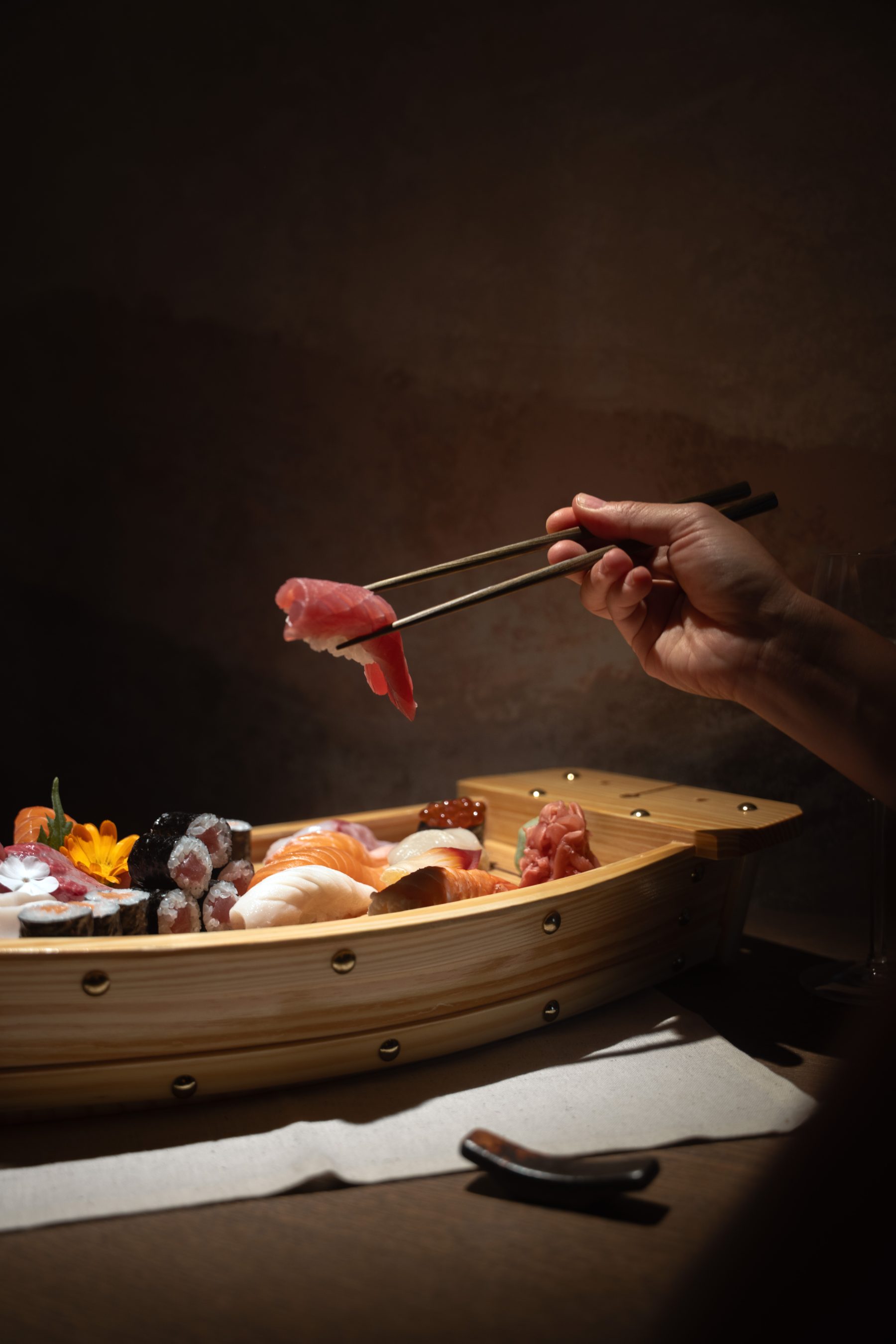 Tuna nigiri lifted with chopsticks from a wooden sushi boat at YAMI