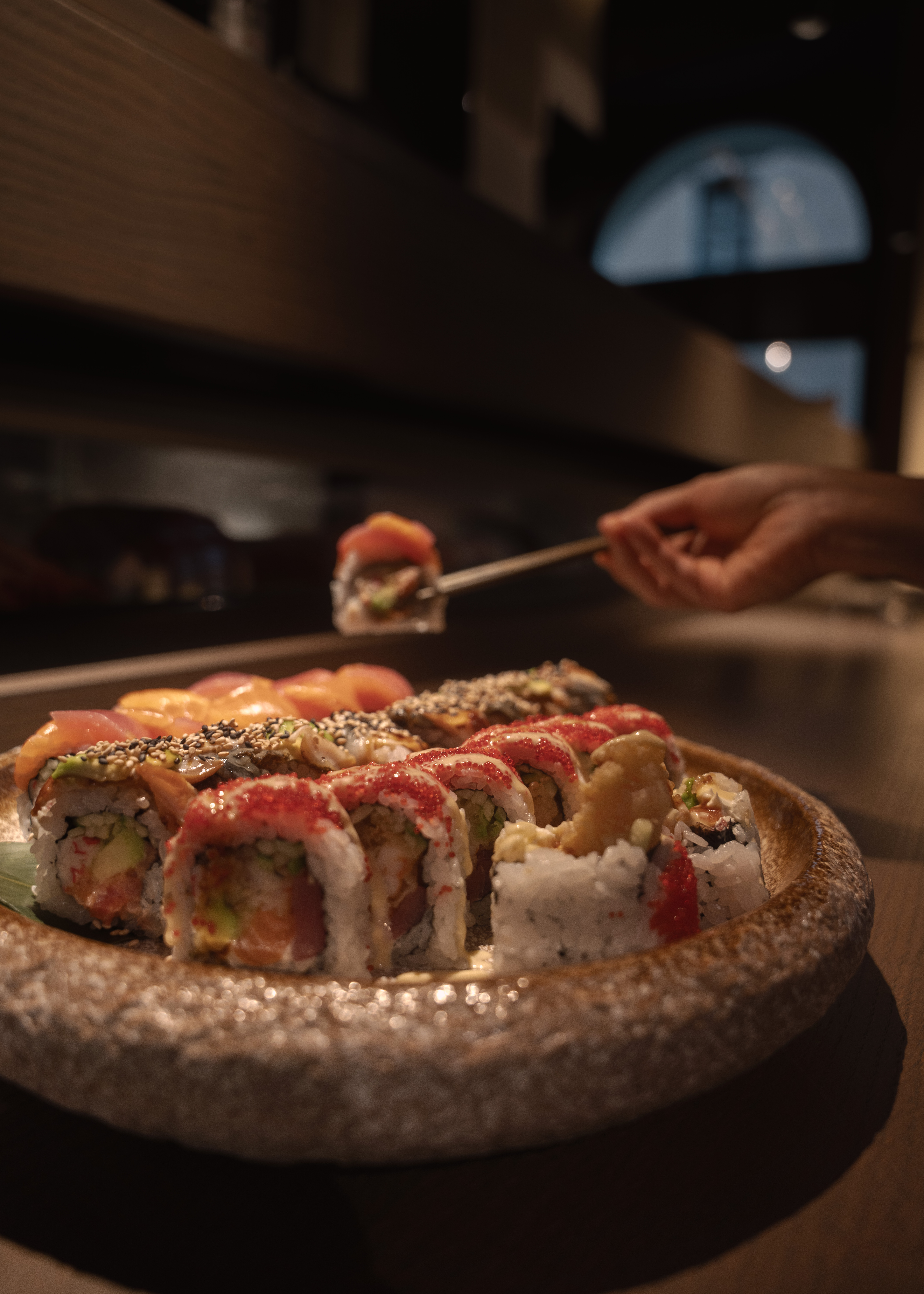 Fusion rolls on a round stone plate, one roll lifted with chopsticks